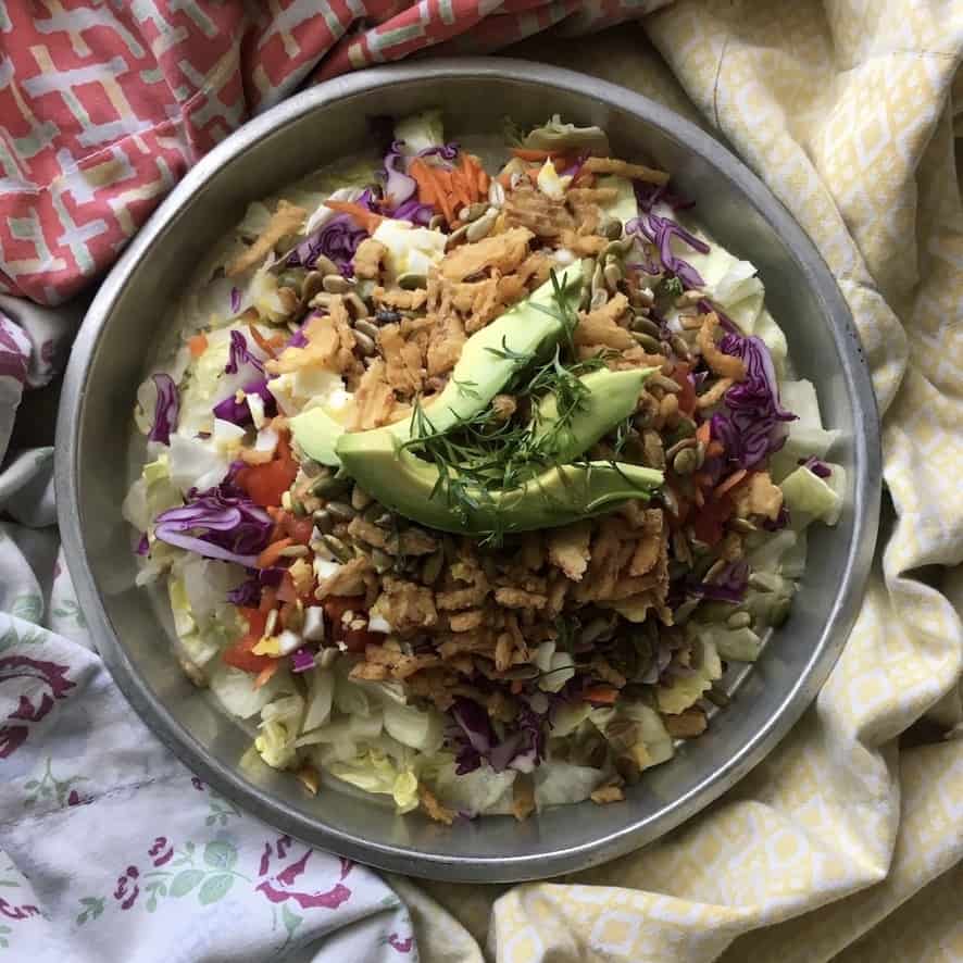 mixed iceberg salad with avocado, french fried onions, carrots, tomatoes, purple cabbage etc. in a shallow vintage round aluminum cake pan lying in the middle of a homemade quilt