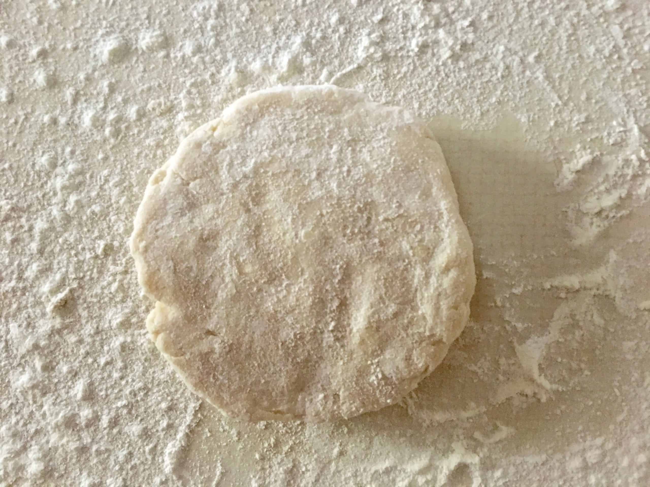the ball of dough fattened into a disc on a floured countertop