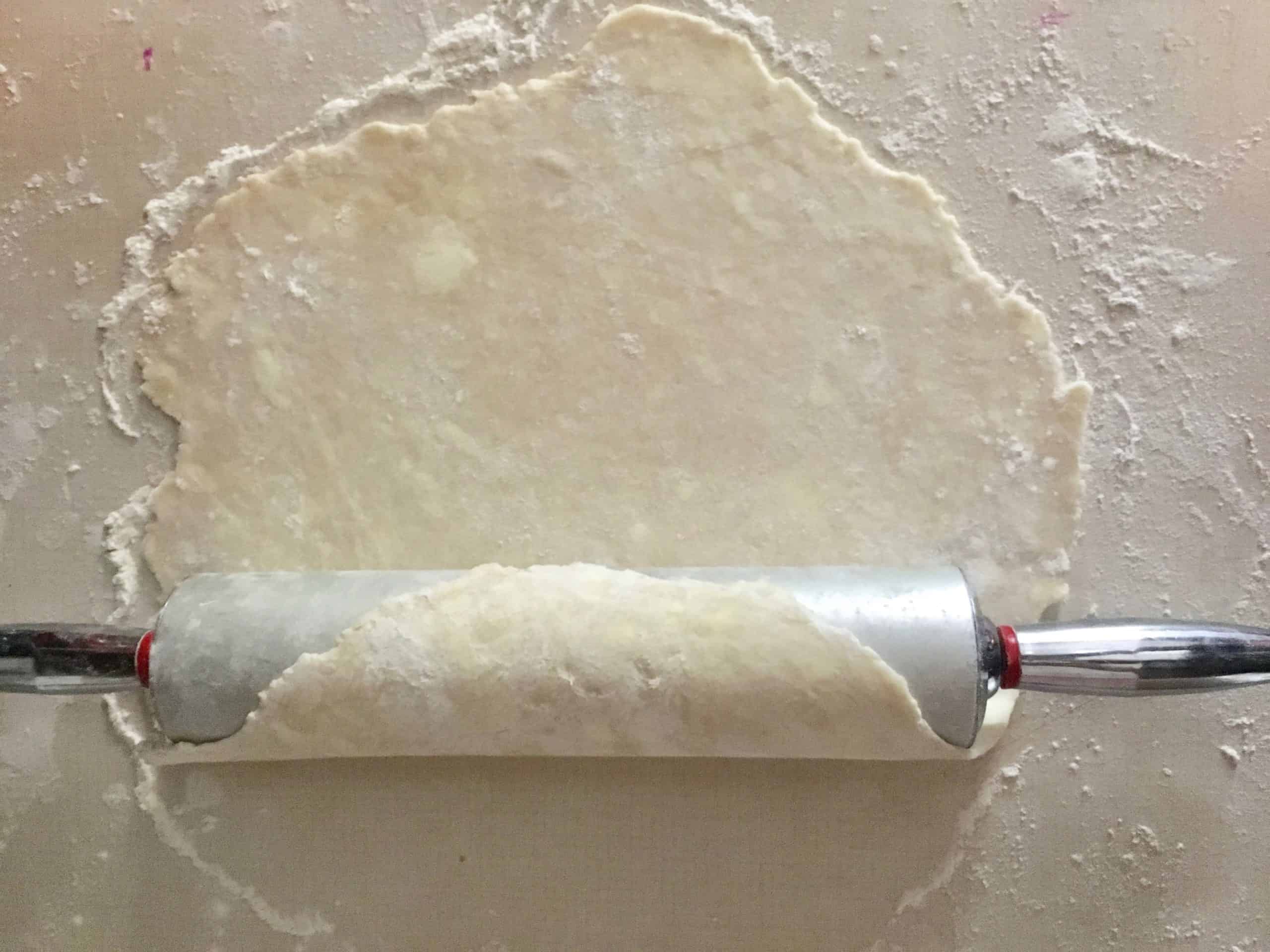 rolling up the rolled out pie dough onto the rolling pin to easily transport it to the pie plate