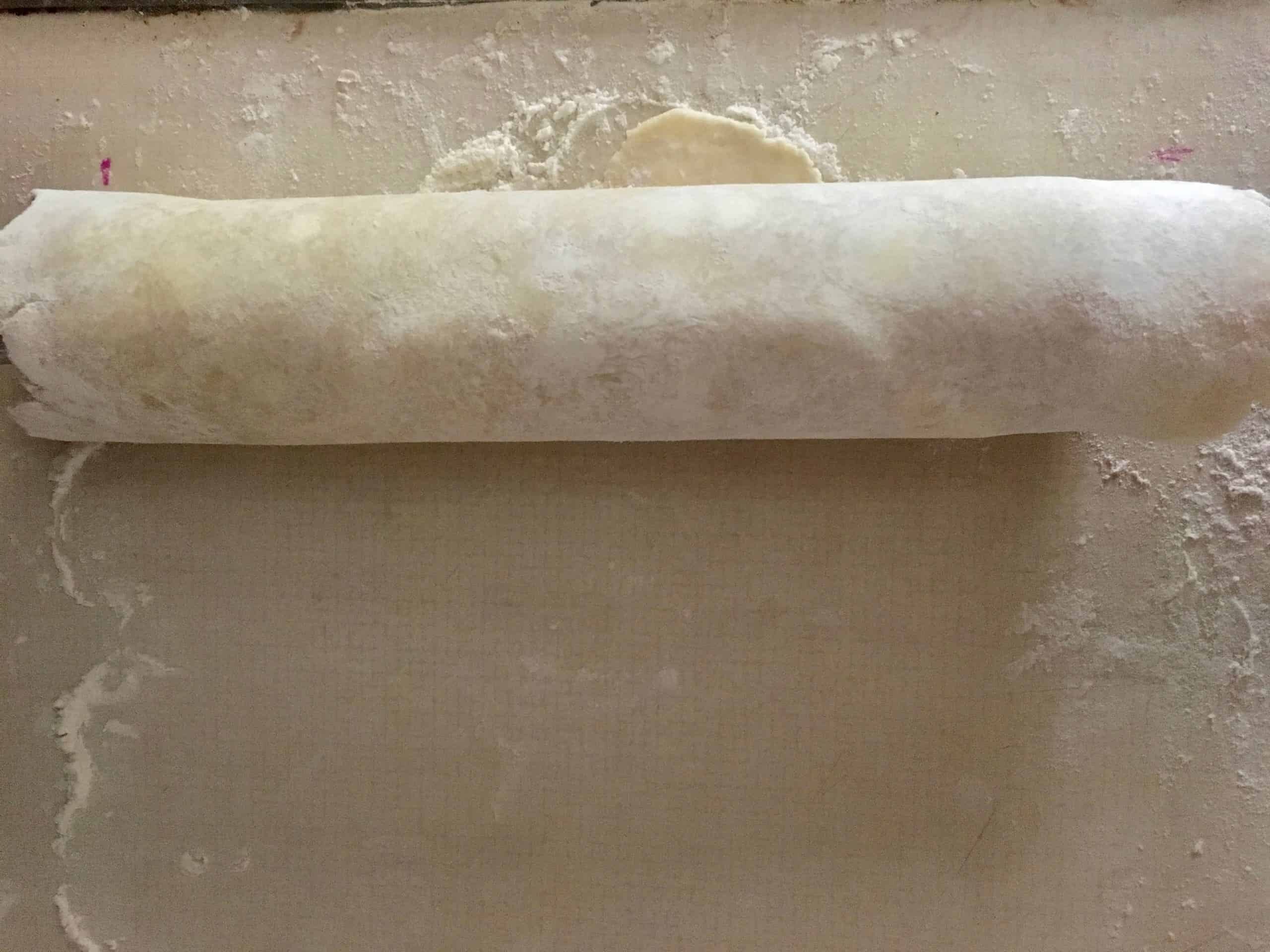 rolled out pie dough rolled completely up onto the rolling pin to easily transport it to the pie plate