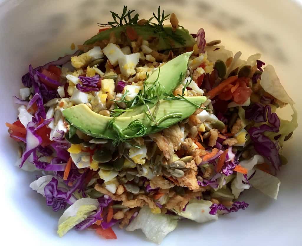 mixed iceberg salad with avocado, french fried onions, carrots, tomatoes, purple cabbage etc. in a shallow vintage round aluminum cake pan lying in the middle of a homemade quilt