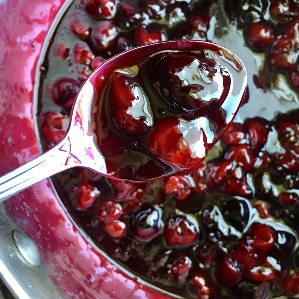 dark sweet cherries combined with bright red sour cherries in this very deep berry colored cherry pie filling on a spoon