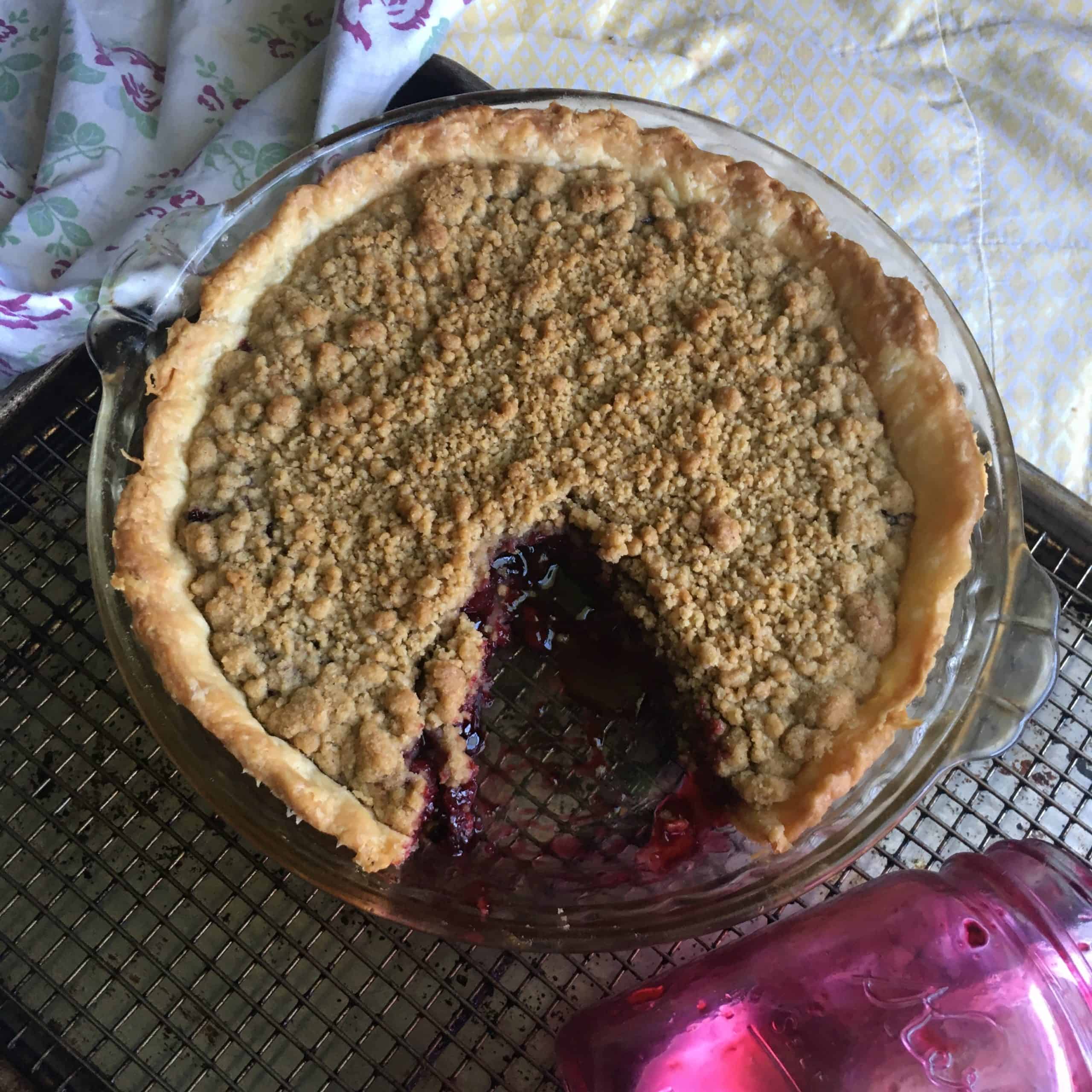 a whole cherry crunch pie with a very large missing piece next to an empty Mason pint jar that's stained pink from the homemade cherry pie filling that was in it