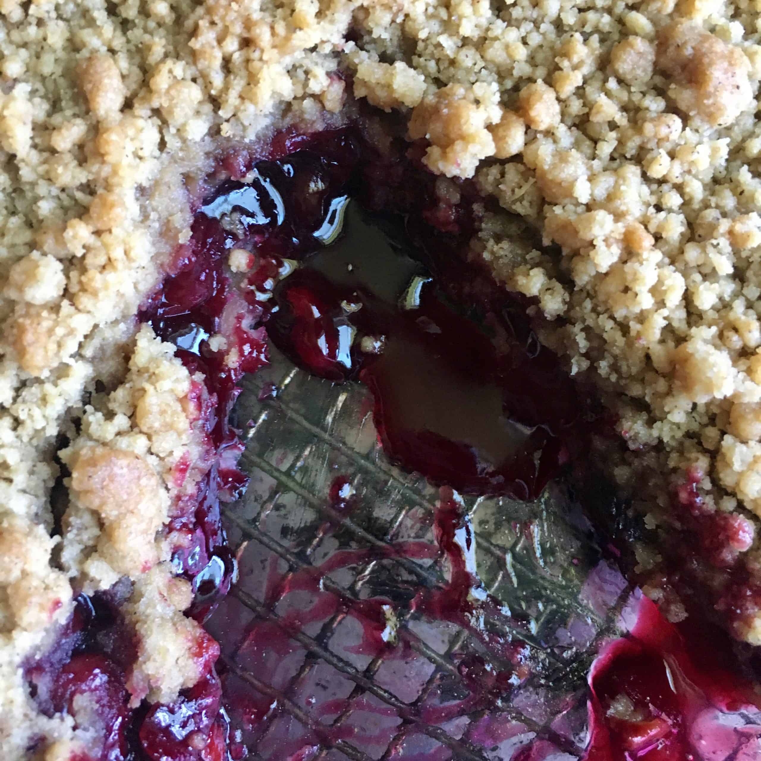closeup of baked cherry crumb crunch pie where a slice has been taken out
