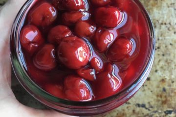 my hand holding a widemouth Mason Jar filled with sweet bright red cherry pie filling