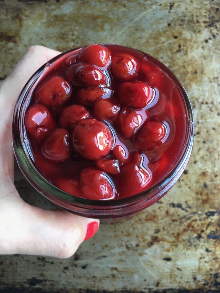 my hand holding a widemouth Mason Jar filled with sweet bright red cherry pie filling