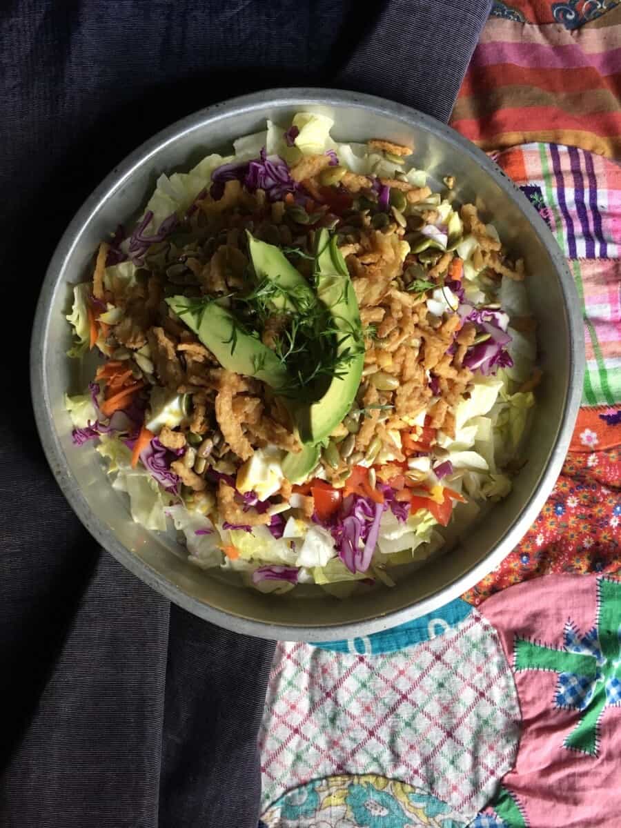salad in a vintage 1 inch cake tin with crispy iceberg, tomatoes, toasted sesame seeds, crunch shredded purple cabbage, crispy fried shallots, and topped with avocado.