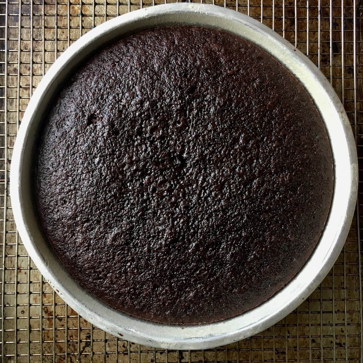 Moist devil's food cake just baked in a round cake pan resting on a cooling rack showing the dark mahogany color of this devil chocolate cake recipe from scratch, the old fashioned devil's food cake that boxed devils food cake mix was based on.