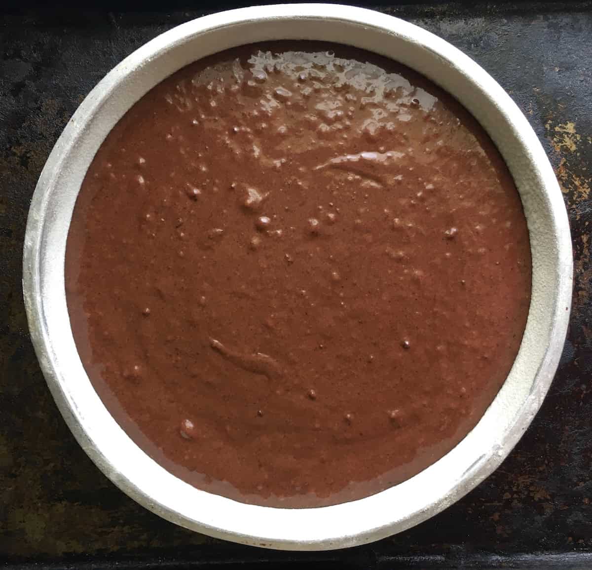 Homemade devil's food cake batter in an 8-inch aluminum cake pan with air pockets removed after tapping, showing the smooth chocolate devil's food batter ready to bake for this old fashioned devil's food cake recipe from scratch.
