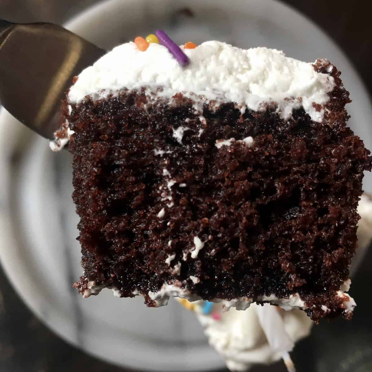 Super moist devil's food cake bite on a fork showing the glistening tender crumb of this homemade double layer devil chocolate cake with fluffy 7-minute frosting, a traditional devil's food cake recipe from scratch.
