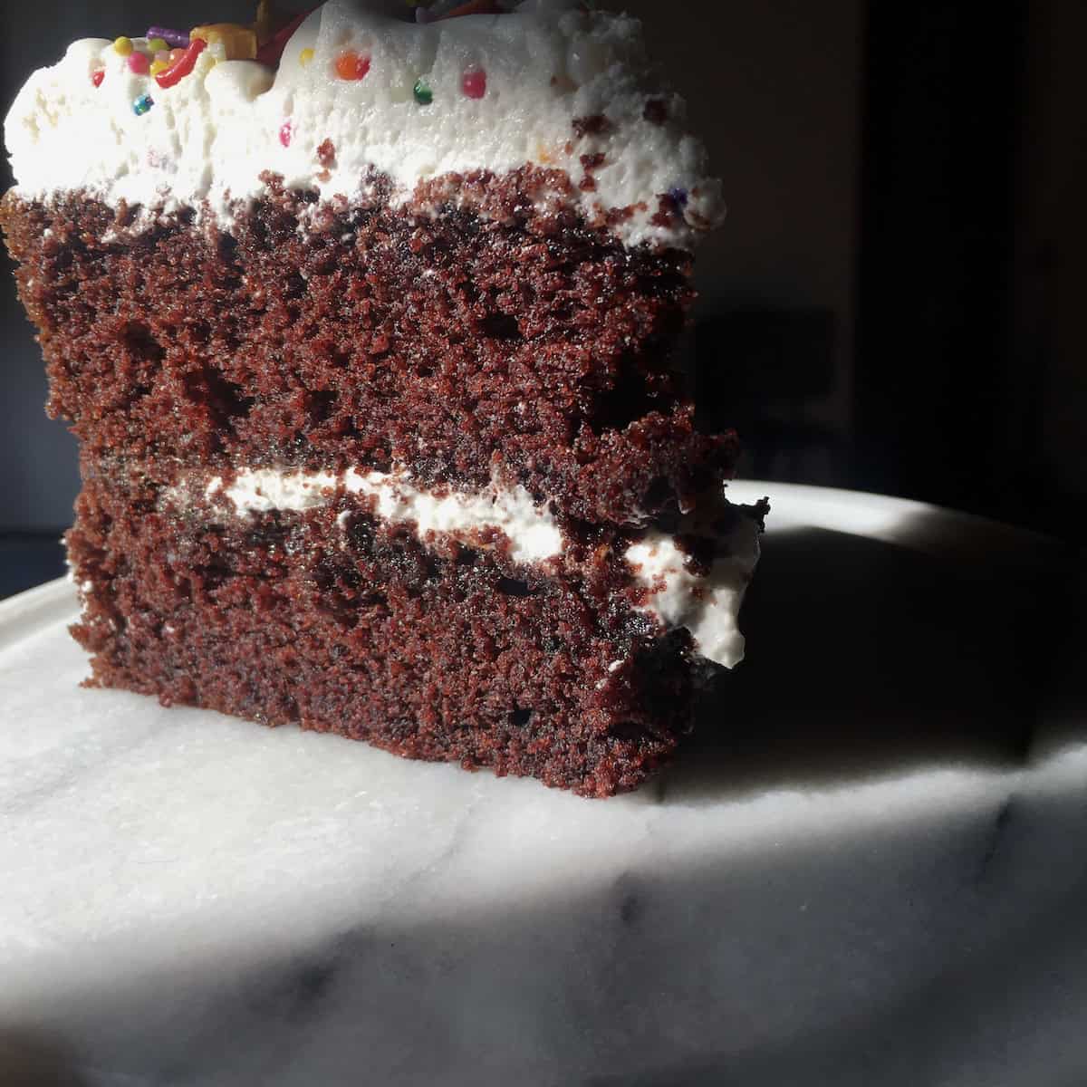 Devil's food cake slice showing the super moist mahogany brown crumb of this homemade double layer cake with fluffy 7-minute frosting and colorful candy sprinkles on top, the best devil's food cake recipe from scratch.

