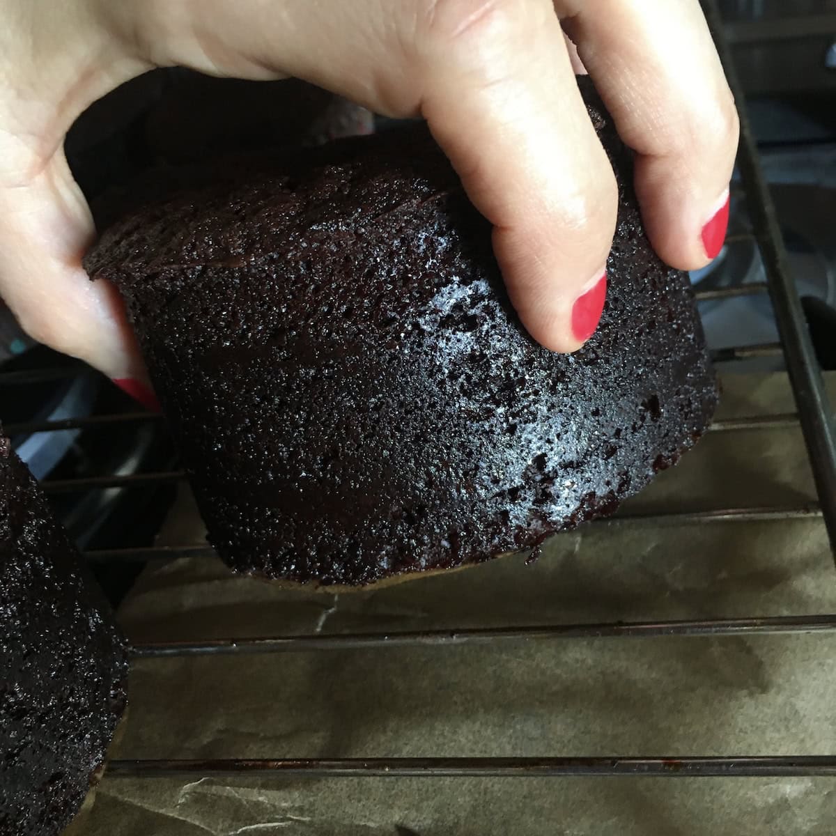 Hand holding a 6-inch super moist devil's food cake mini cake  showing the glistening sides and intensely moist crumb of this devil food cake made from scratch, showing what makes devil's food cake different than regular chocolate cake.

