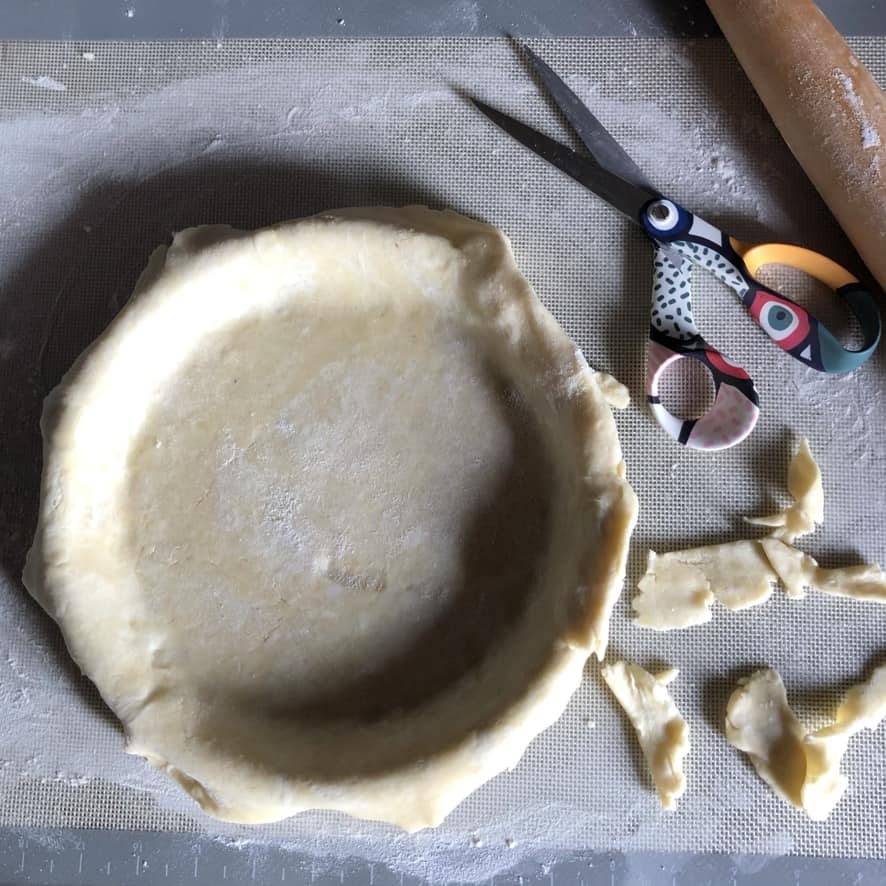 a pie dough being trimmed after being put in the pie plate