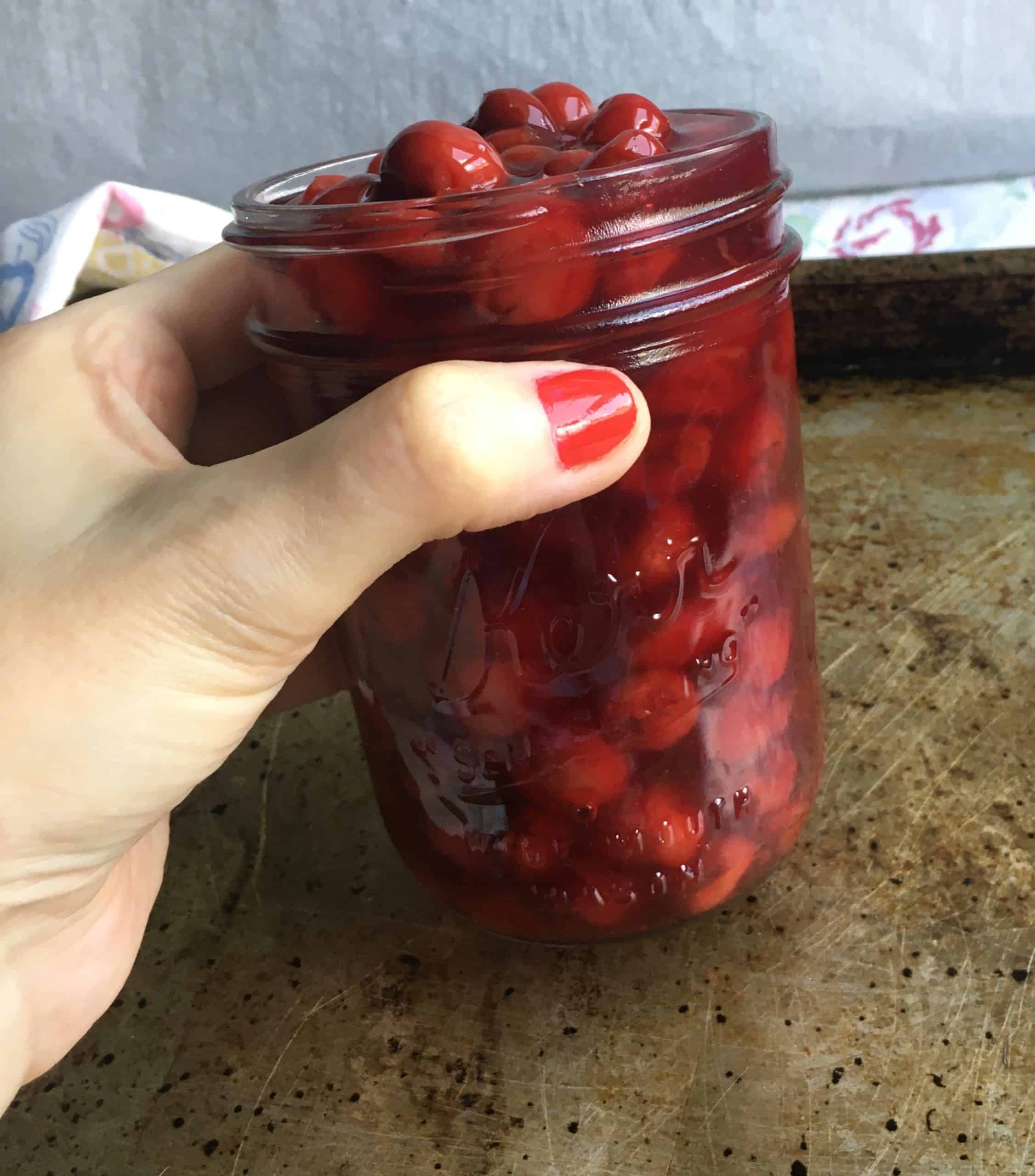 my hand holding a mason jar filled with homemade cherry pie filling