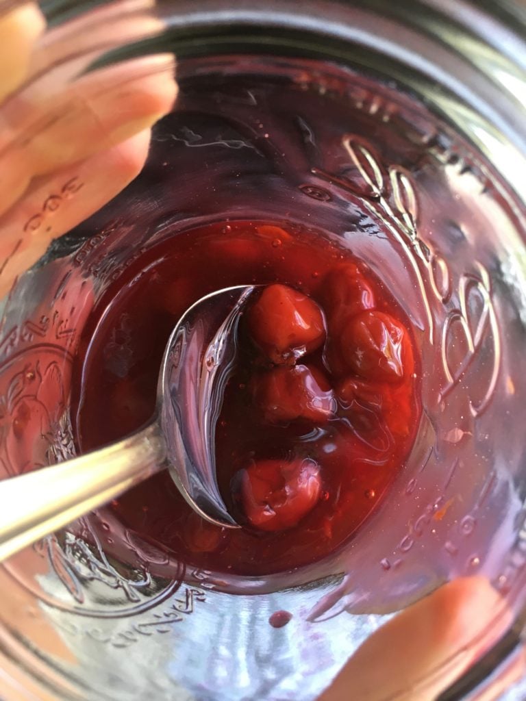 a mason jar with some cherry pie filling in it with a view down into the jar with a spoon in it