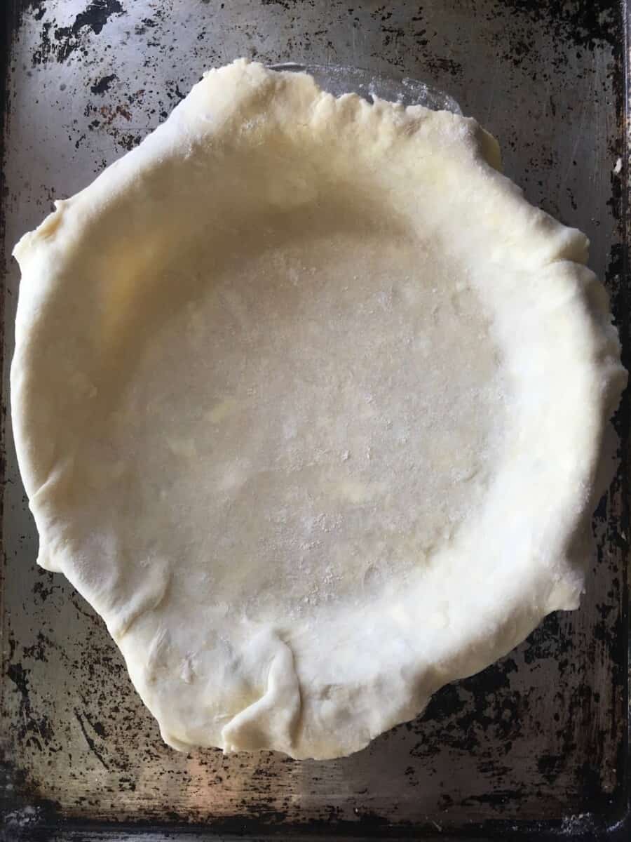 pie dough draped over a pie plate before being trimmed