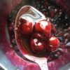 a perfect spoonful of dark and bright red cherry pie filling on a silver serving spoon being held above the pot with the rest of the cherry pie filling below