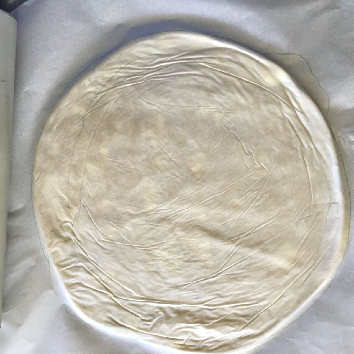 a rolled out pie dough with parchment paper on top ready to be placed into the pie plate and chilled