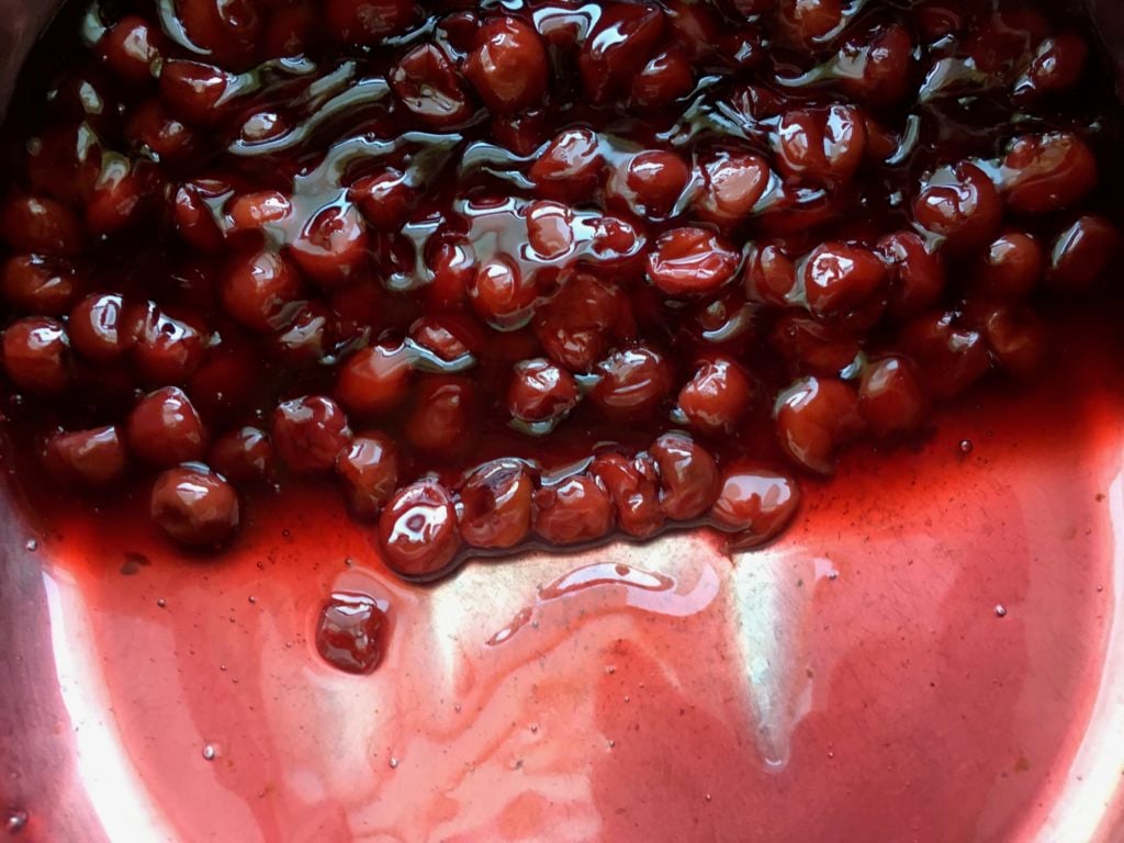 A pot full of fresh sour cherry pie filling glistening and looking beautifully cherry red.