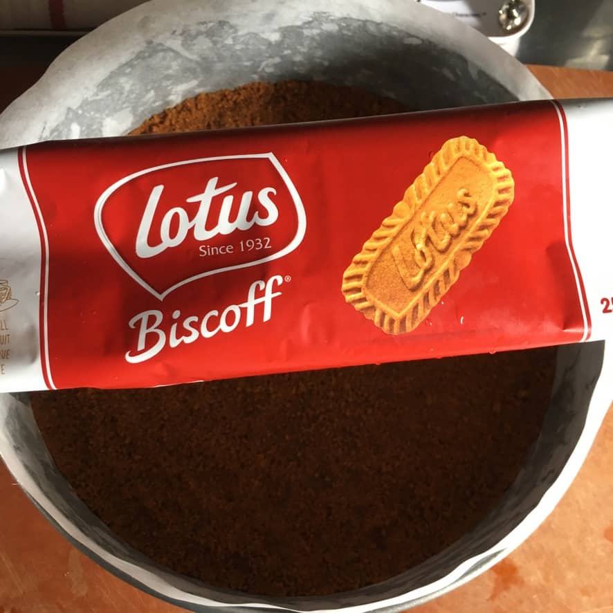 a package of Lotus Biscoff Cookies with its bright red and white package sitting atop a prepared springform pan with Biscoff cookie crust inside about to be baked