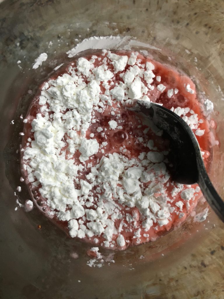 Stawberry rhubarb juice with cornstarch added being mixed together with a spoon to make the cornstarch slurry.