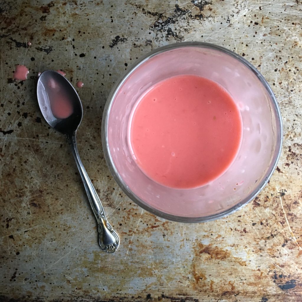 a totally lump-free strawberry-rhubarb cornstarch slurry mixture with a spoon lying next to the small glass prep bowl