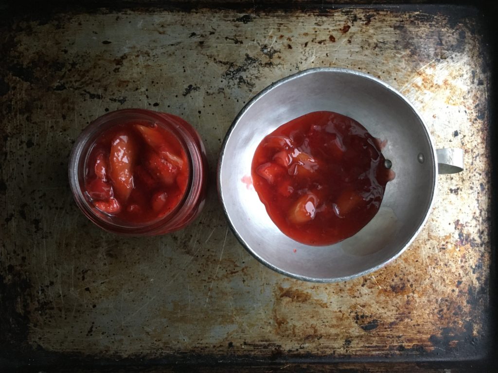 top down view of two mason jars (one pint and one half-pint) of strawberry rhubarb pie filing (one with a vintage aluminum funnel in the jar)