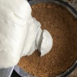 pouring in the cream cheese base to the prepared graham cracker crust