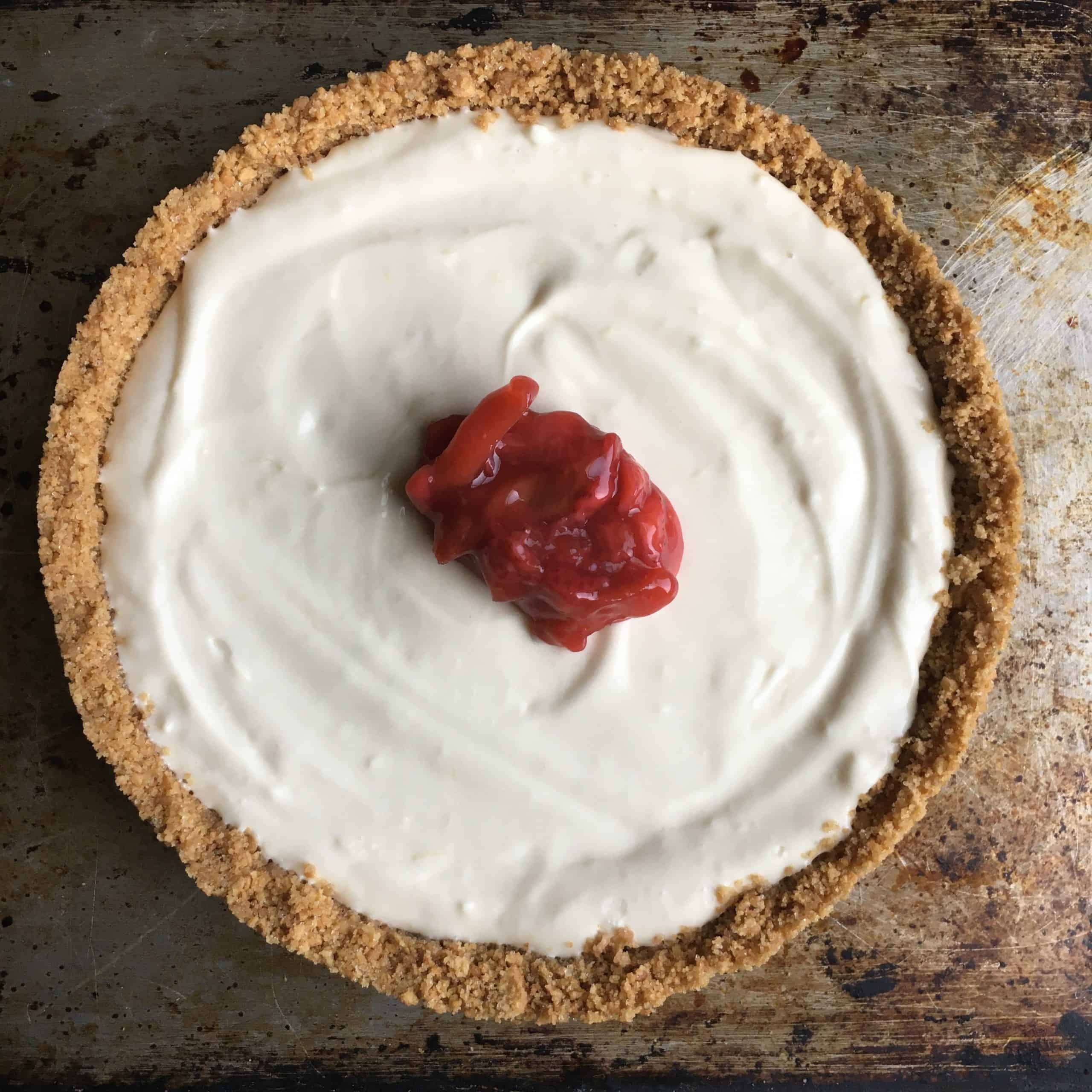 a whole strawberry rhubarb pie with one dollop of the pie filling in the center only baring it's white creamy filling and graham cracker sides