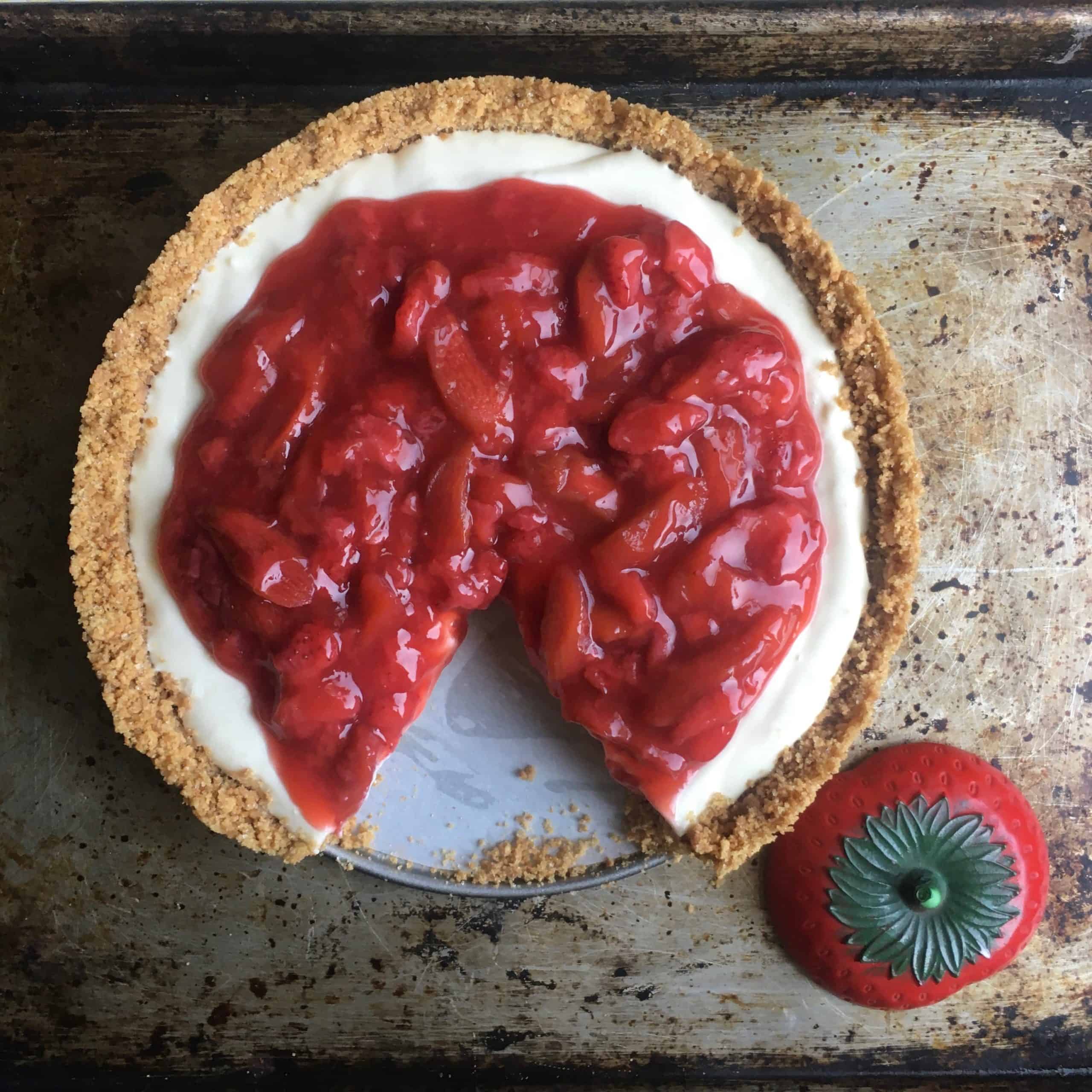 closeup of strawberry rhubarb pie with a slice removed revealing it's creamy tangy filling with a ceramic strawberry lying next to it (top down view)