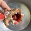 my hand holding a cherry fried pie wonton with a bite taken out and it's gloriously cherry red filling exposed inside