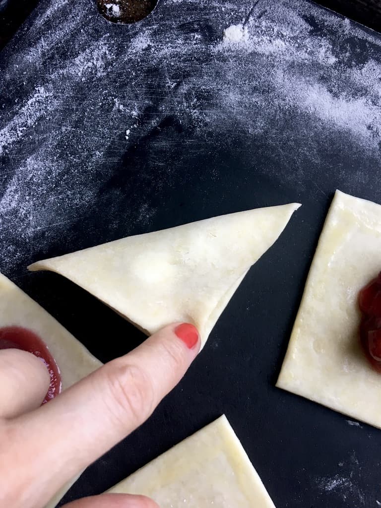 using my finger to show how to seal the triangular piece of fried pie dough filled with cherry pie filling