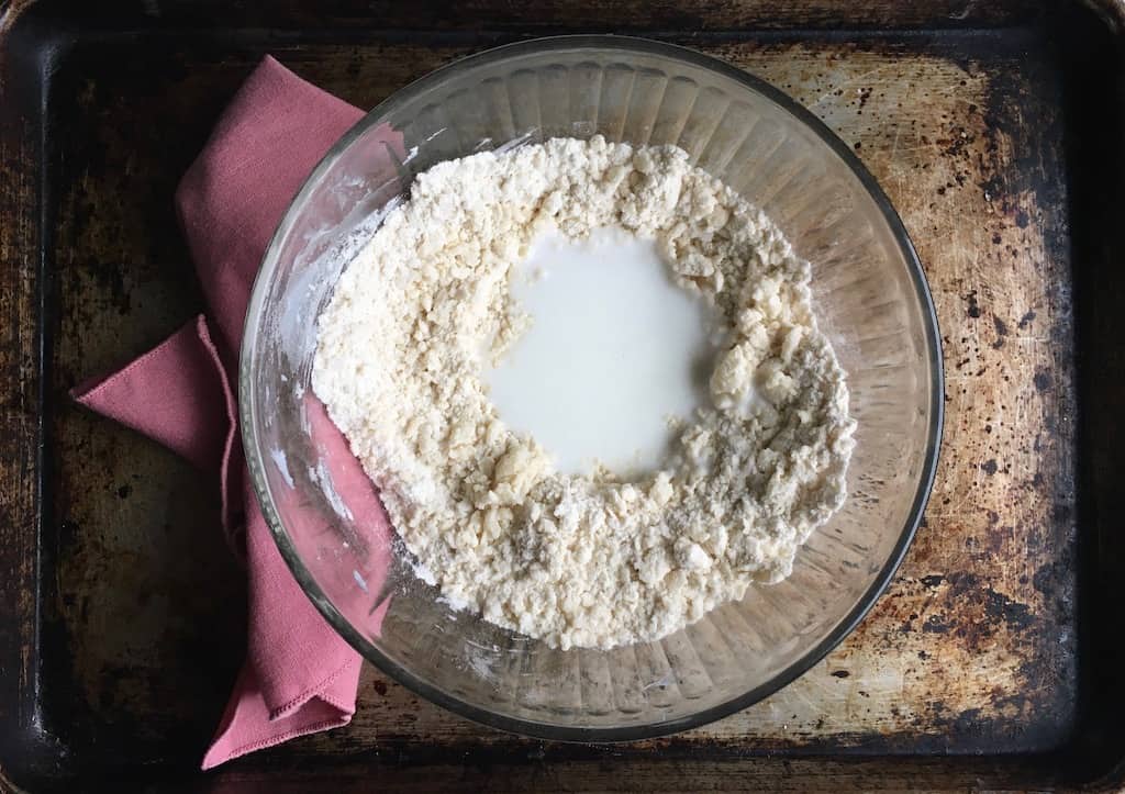 glass mixing bowl with fried pie ingredients blended and buttermilk added in it and a pink napkin lying next to it on the left on top of a sheet pan