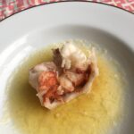 a tender cooked and slightly curled fresh lobster tail sitting in a pasta bowl of clarified butter