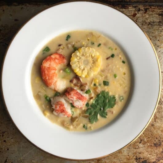 top down view of a bowl of corn chowder with lobster tail, sliced corn on the cob piece with an argentinian royal red shrimp and sprinkling of chives and parsley