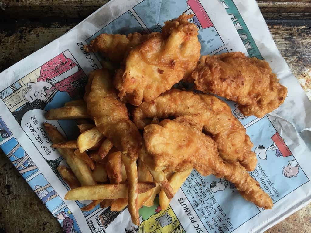 extra crispy fried chicken tenders with french fries lying on the comic section of the newspaper