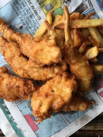 A large pile of light and crispy beer-battered chicken tenders (chicken fingers copycat recipe of Chili's Chicken Crispers with twice fried french fries on top of the sunday comics newspaper section.