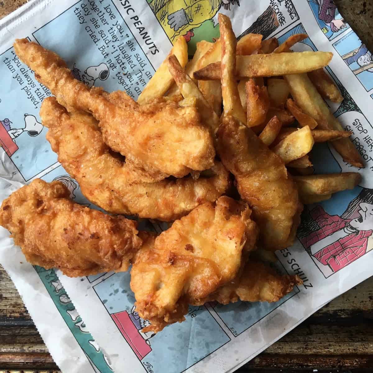 A large pile of light and crispy beer-battered chicken tenders (chicken fingers copycat recipe of Chili's Chicken Crispers with twice fried french fries on top of the sunday comics newspaper section.