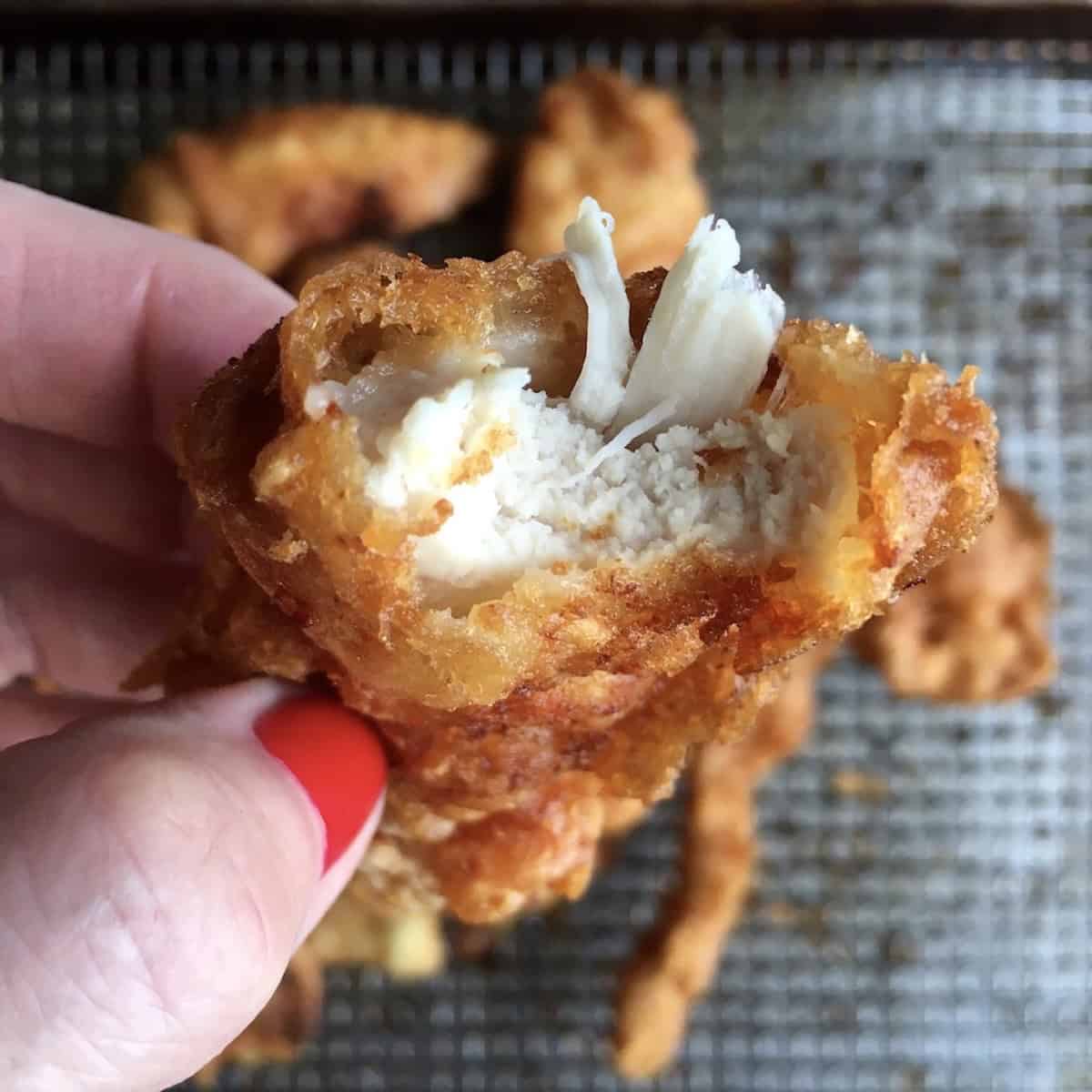 Bite taken from crispy fried chicken tender revealing juicy chicken breast meat inside showing best homemade chicken tenders recipe results.
