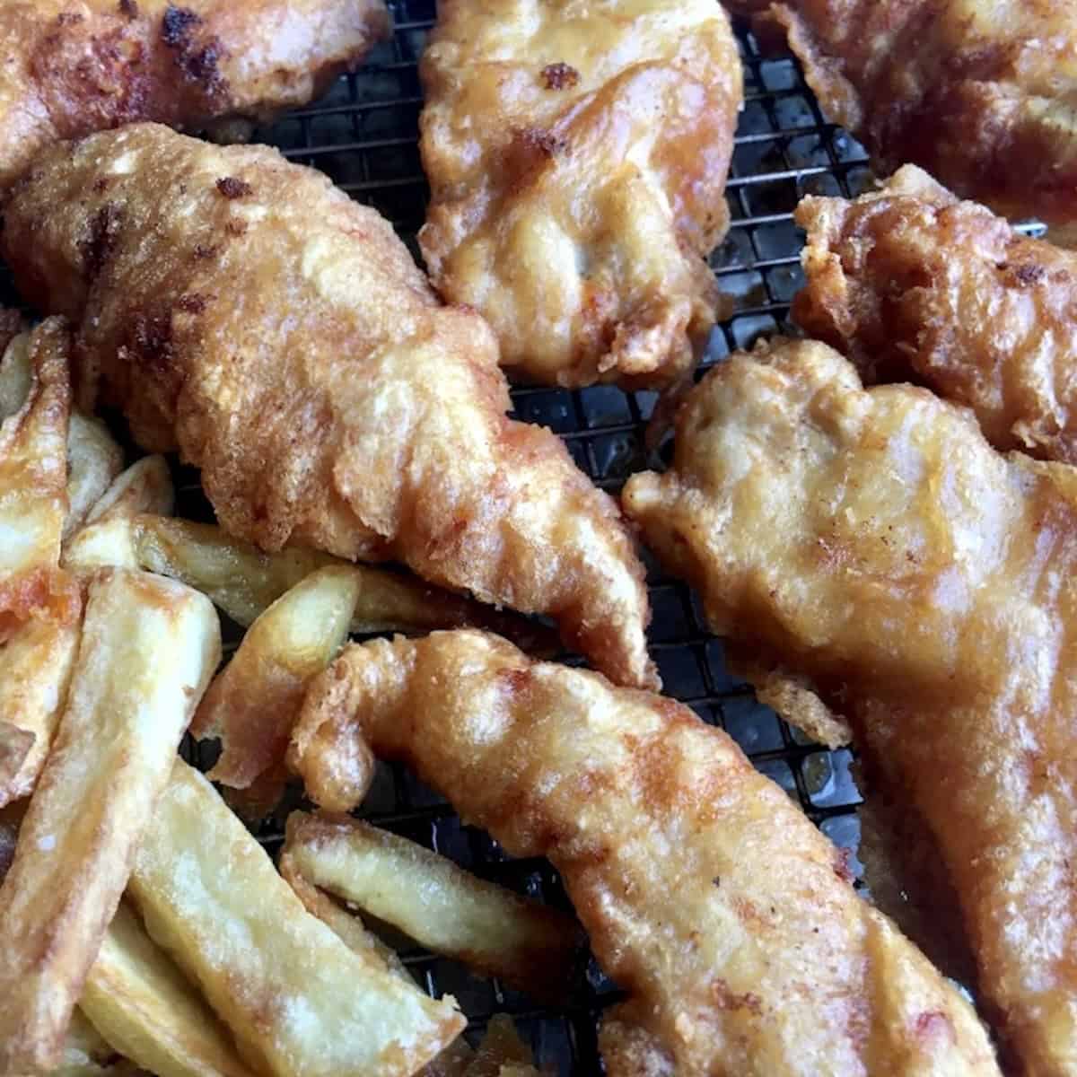 Pile of extra crispy fried chicken tenders with homemade twice fried french fries showing best homemade chicken tenders recipe served with fries.