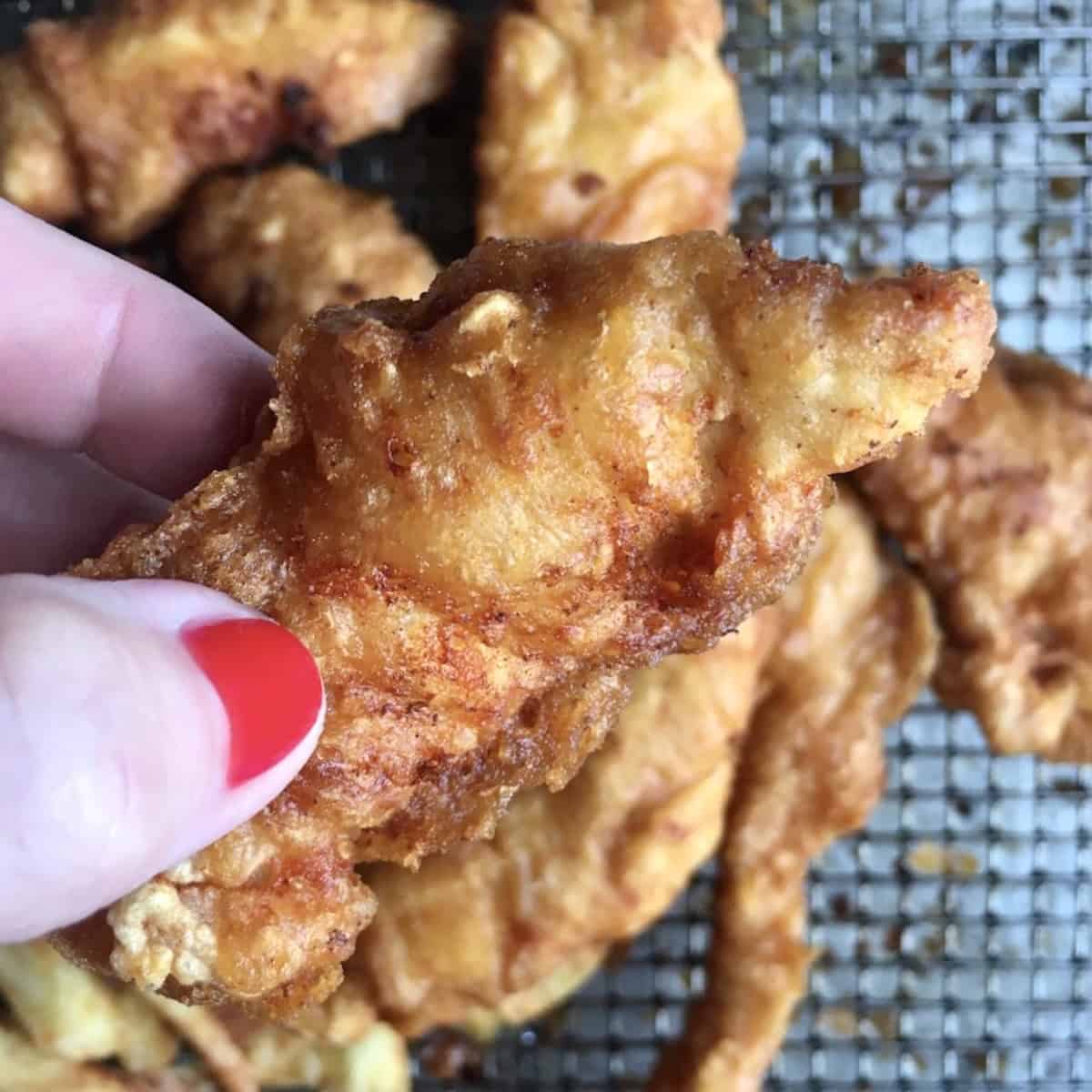Crispy fried chicken finger held up showing crunchy batter-dipped coating for best chicken crispers recipe homemade copycat style.