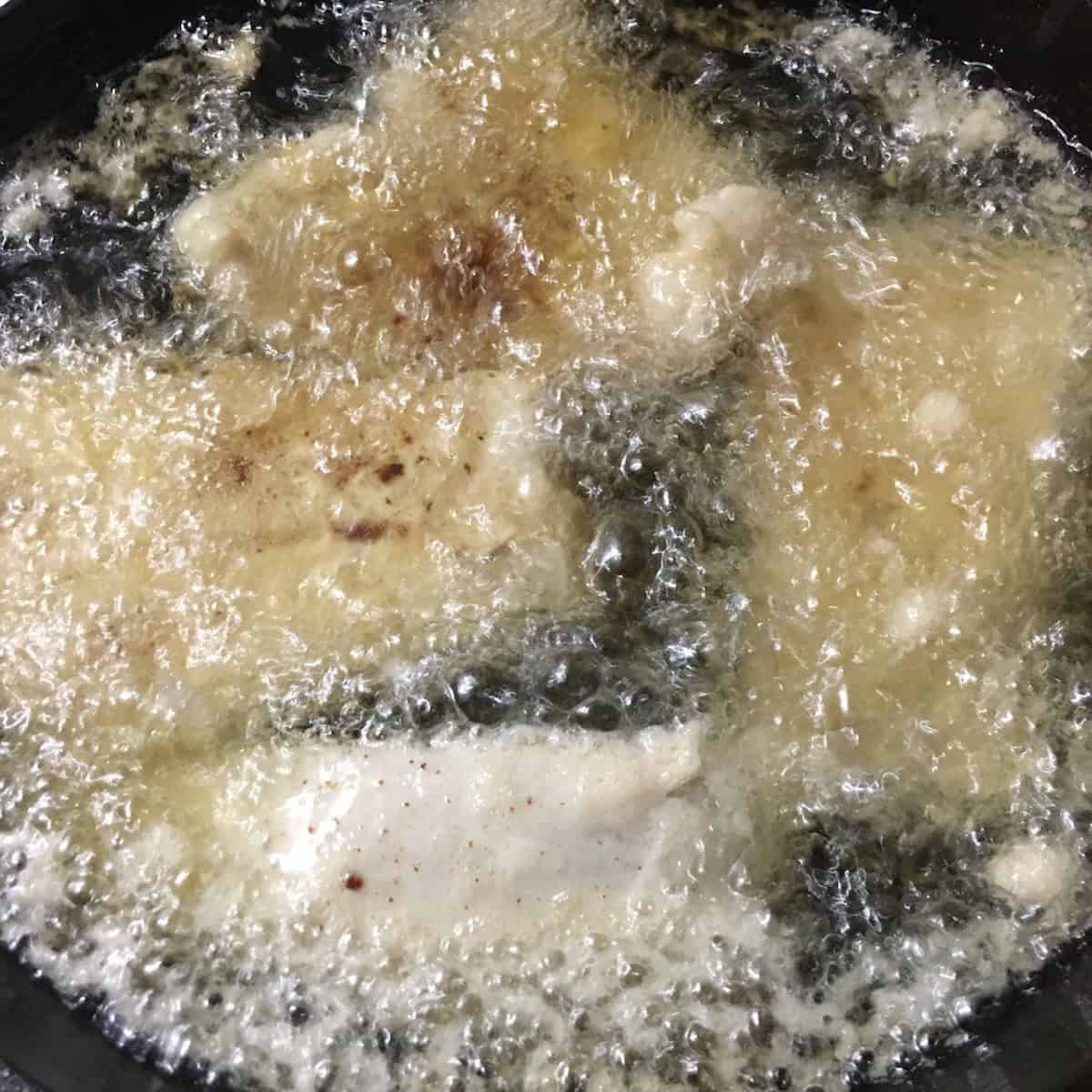 Beer battered chicken tenders frying in cast iron skillet with hot oil showing how to make crispy fried chicken tenders homemade recipe.
