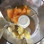 pouring chicken broth into the food processor with garlic and orange (or clementine)