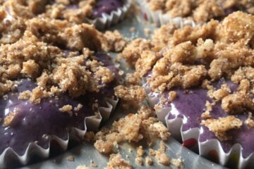 purple very berry muffin batter in foil cupcake liners in a muffin tin covered with crunchy sugar crumb topping just before baking