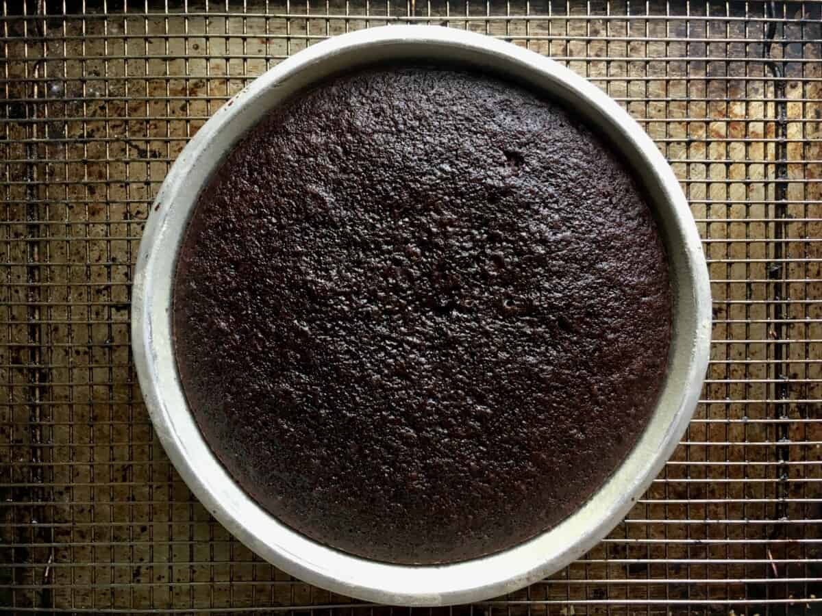 8 inch baked devil's food cake cooling on a wire rack and appearing almost black like the color of an Oreo cookie it's so dark and decadent after baking