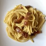 spaghetti carbonara plated in a white pasta bowl with rectangular pieces of beautifully browned pancetta throughout