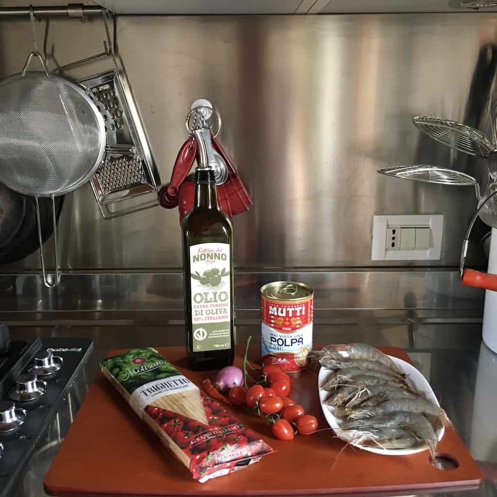 shrimp pasta ingredients on wooden cutting board next to stove on stainless steel countertop