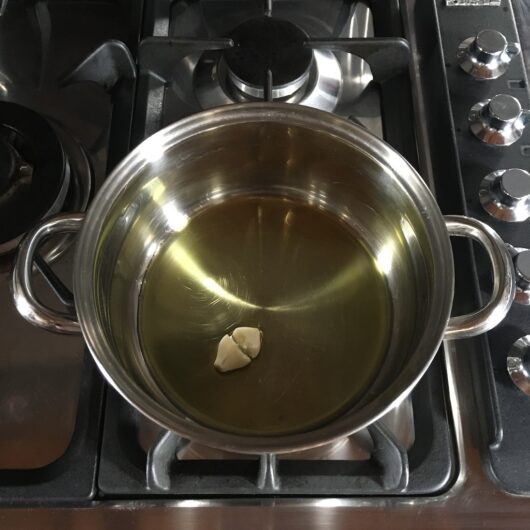 blistering a garlic clove in a stainless steel pot in extra virgin olive oil