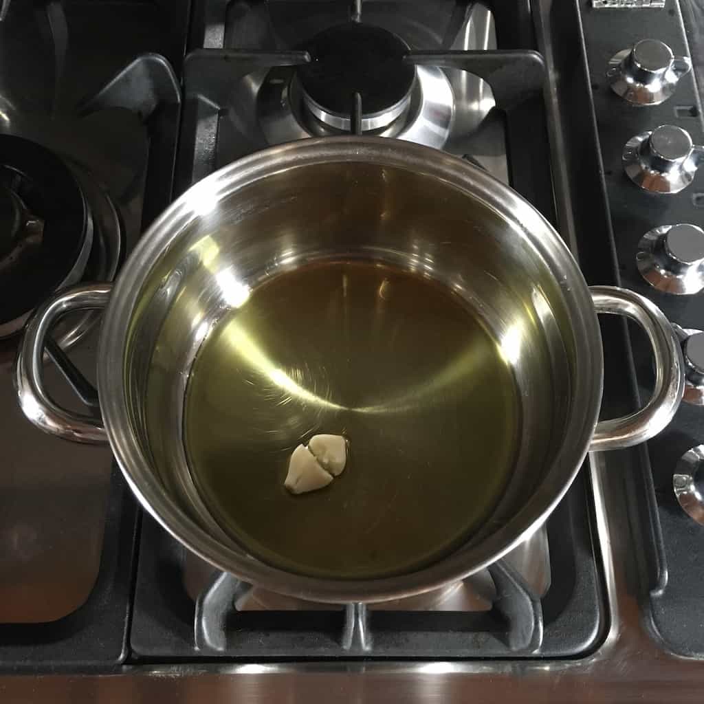 blistering a garlic clove in a stainless steel pot in extra virgin olive oil