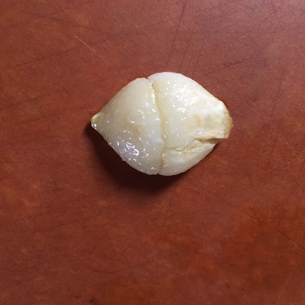 Blistered garlic clove on cutting board after being shallow fried in olive oil.